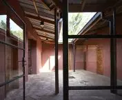 Enclosed courtyard with terracotta walls, stone tile floor, wooden doors and a partially covered roof supported by metal columns