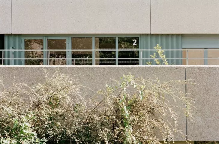 Modern building facade with ribbed panels, rectangular windows and surrounding vegetation