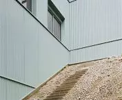 Betonowe schody obok budynku z jasnozieloną okładziną i prostokątnymi oknami