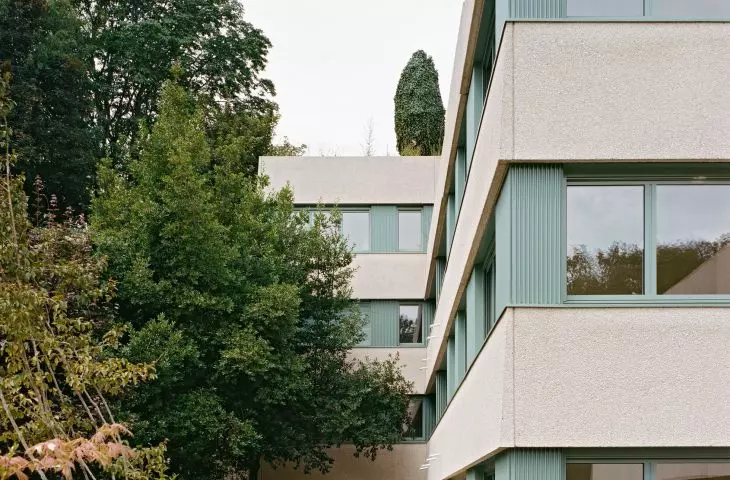 Nowoczesny budynek z beżowo-turkusową fasadą i dużymi oknami