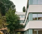 Nowoczesny budynek z beżowo-turkusową fasadą i dużymi oknami