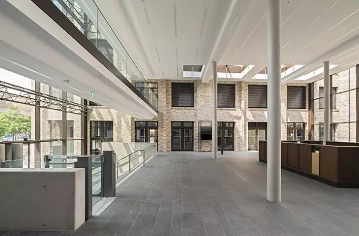 Nowoczesne atrium z wysokimi sufitami, świetlikami i antresolą ze szklanymi balustradami, z podłogą wyłożoną szarymi kafelkami