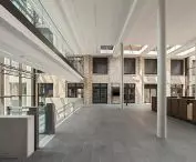 Modern atrium with high ceilings, skylights and a mezzanine with glass balustrades, with gray tiled floor