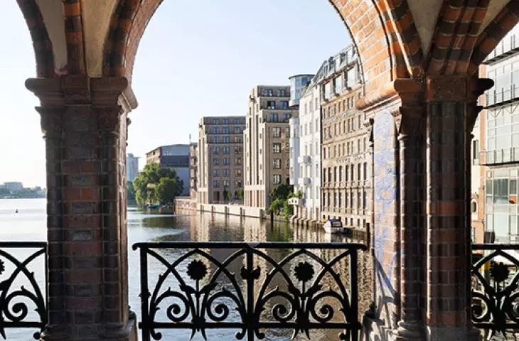 View through a brick arch with decorative railings, overlooking the river and city buildings