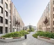 A modern courtyard between two rows of tall brick buildings with cobblestone paths and green plants in between