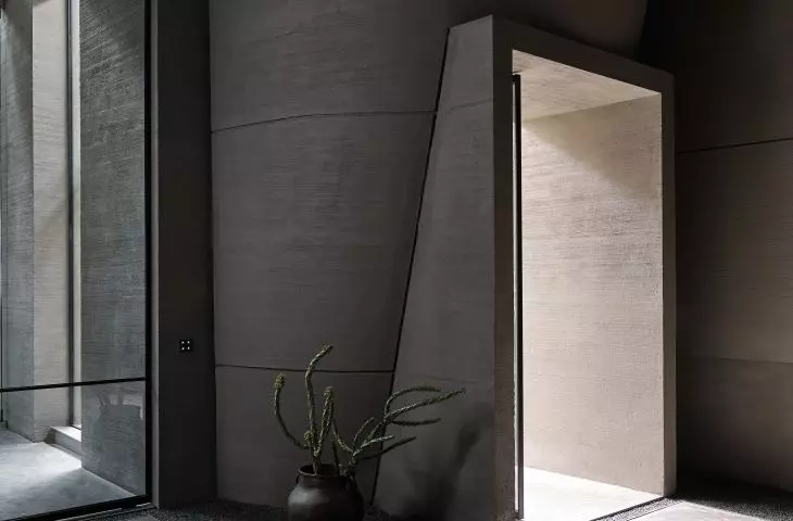 Minimalist interior with concrete walls, a large window, a cactus in a ceramic pot and a pebbled floor