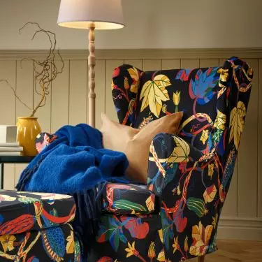 An earlobe armchair with a cover in a pattern of multicolored autumn leaves is the perfect choice for long evenings with a book