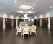 Nowoczesna sala konferencyjna z długim stołem i jasnymi drewnianymi krzesłami pod kulistą lampą wiszącą