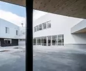 Nowoczesny dziedziniec budynku z białymi ścianami, dużymi oknami i drewnianymi sufitami