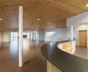 Przestronny, nowoczesny przedpokój z drewnianym sufitem i zakrzywioną ladą oraz białym filarem