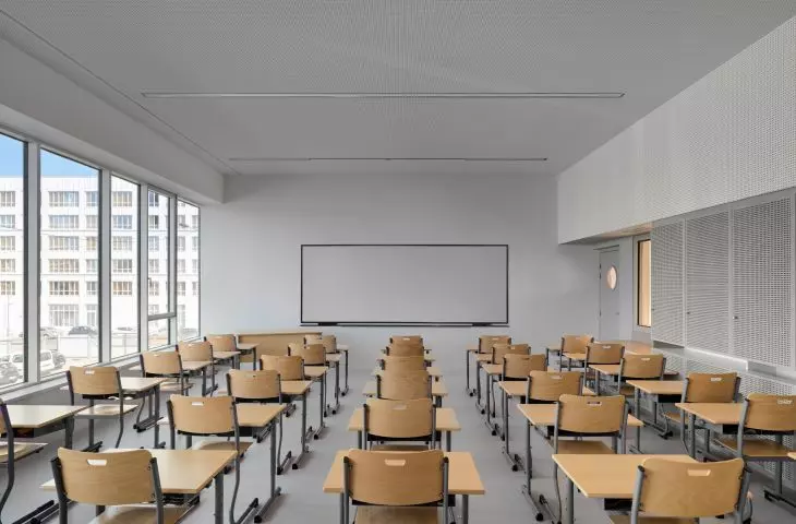 Nowoczesna sala lekcyjna z drewnianymi biurkami i krzesłami, dużymi oknami i tablicą