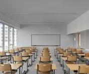 Nowoczesna sala lekcyjna z drewnianymi biurkami i krzesłami, dużymi oknami i tablicą