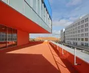 Modern building with orange terrace and walls and blue upper facade with large windows