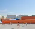 Children playing with a hula-hoop and a ball in a school playground with orange walls 