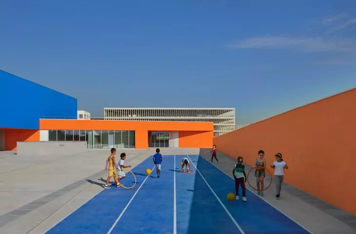 Children playing on a blue path next to a colorful modern building and an orange wall