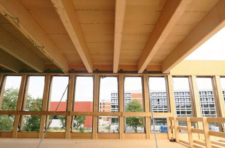 Interior view of the construction site with wooden beams, unglazed windows and a view of the modern building outside