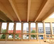 Interior view of the construction site with wooden beams, unglazed windows and a view of the modern building outside