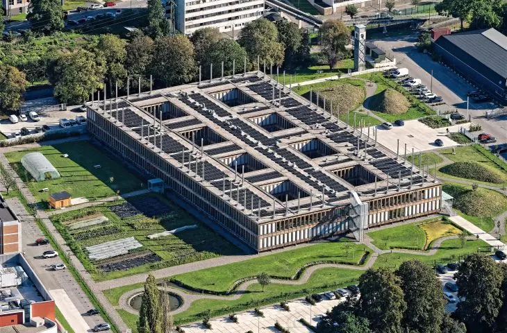 Aerial view of a modern rectangular building with eight courtyards, surrounded by greenery and urban structures