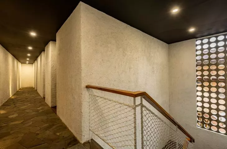 Widok wnętrza nowoczesnego korytarza z kamienną podłogą, wbudowanym oświetleniem i schodami z siatkową balustradą