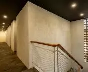 Widok wnętrza nowoczesnego korytarza z kamienną podłogą, wbudowanym oświetleniem i schodami z siatkową balustradą