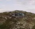 Nowoczesny dom z przeszklonym frontem wbudowany w skaliste wzgórze otoczone naturalną roślinnością