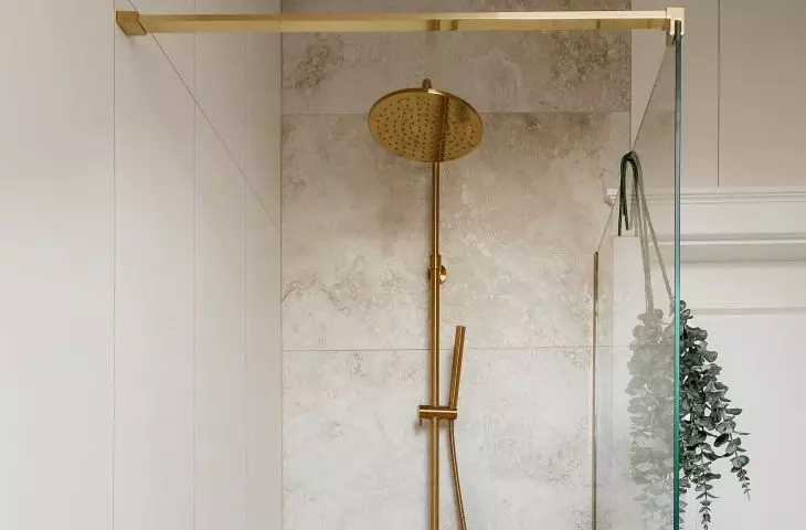 The walk-in shower consists of a sheet of tempered glass and a gold bracket