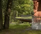 Historyczny dwór w Poniewieżu — widok na historyczny budynek z czerwonej cegły i nową konstrukcję schowaną pod ziemią 