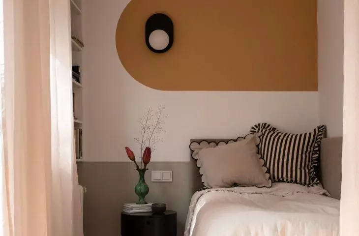 The wall behind the bed is decorated with a mural in a mustard shade