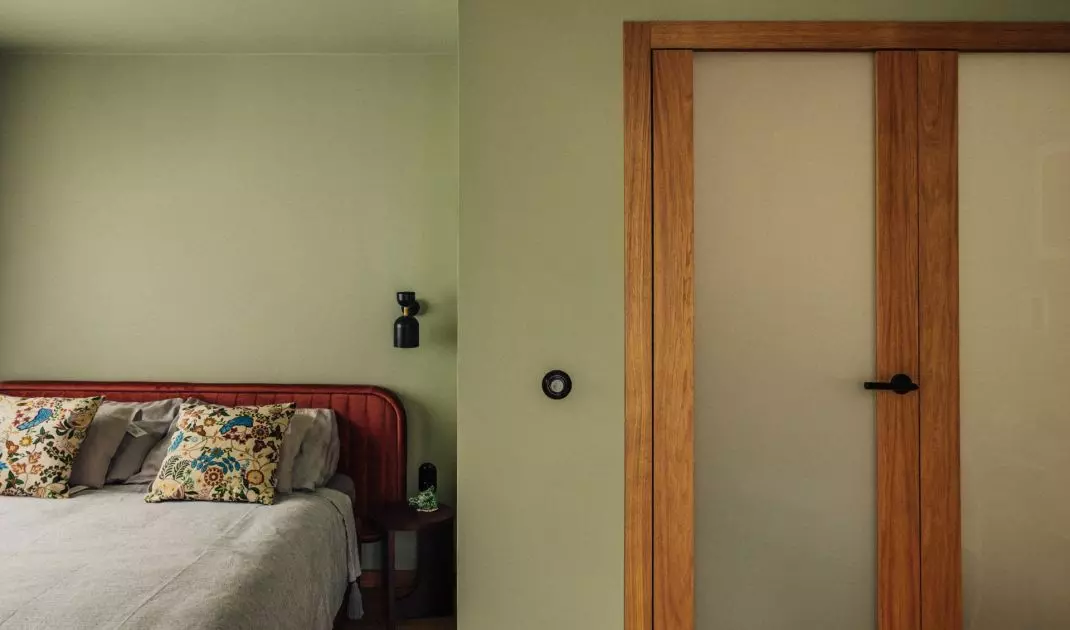 Sage shade of the walls contrasts with the brick-red bed headboard