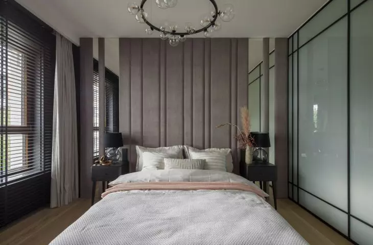 The wall behind the bed is covered with upholstered panels interspersed with mirrored sections
