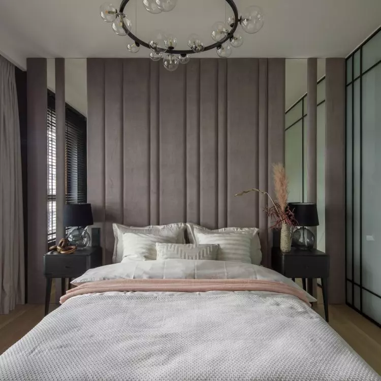 The wall behind the bed is covered with upholstered panels interspersed with mirrored sections