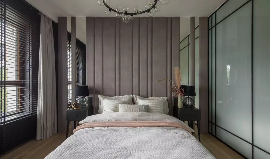 The wall behind the bed is covered with upholstered panels interspersed with mirrored sections