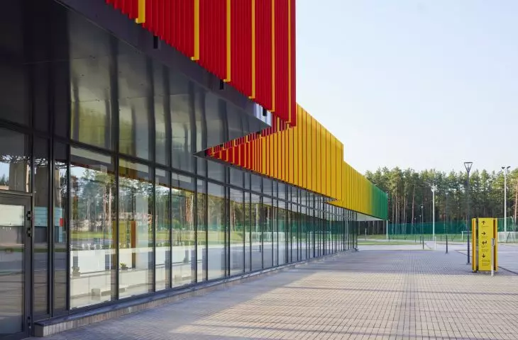 Training center for athletes in Druskininkai, Lithuania - the first floor of the facility has been glazed, while the higher parts of the building are distinguished by a colorful facade strip of narrow vertical slats