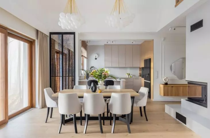Upholstered light-colored chairs with contrasting black legs were placed at a large wooden table