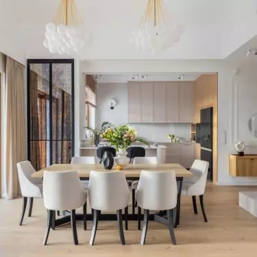 Upholstered light-colored chairs with contrasting black legs were placed at a large wooden table