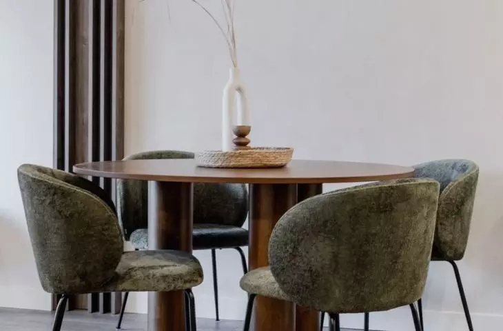 The round wooden table is surrounded by upholstered chairs in a shade of deep green
