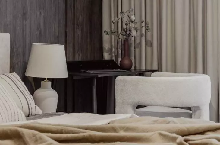 Next to the bed, a work area has been arranged with a simple desk and an armchair made of soft bouclé fabric