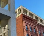 z ceglanym fragmentem szkoły wciągniętym w kubaturę jednego z budynków kontrastuje rytmiczna struktura betonowej kraty