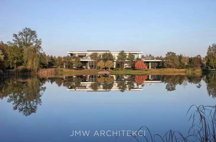 Lakefront Residence is located directly on the water, making the surface of the pond reflect the body of the building, the surrounding vegetation and the sky