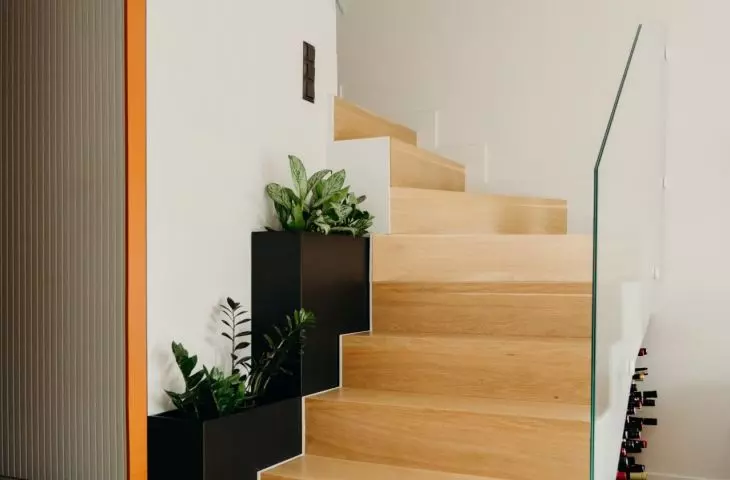 The wooden staircase is complemented by a modern balustrade made of transparent glass