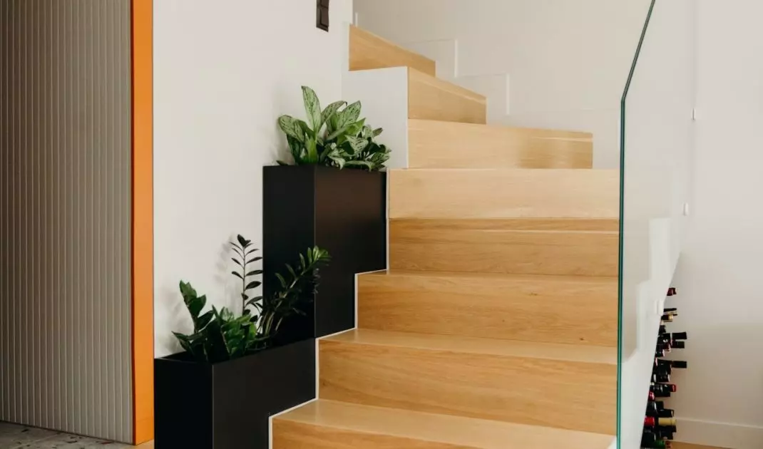 The wooden staircase is complemented by a modern balustrade made of transparent glass