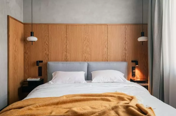 The bed is set against a high wooden wall, which visually warms the raw base of the bedroom