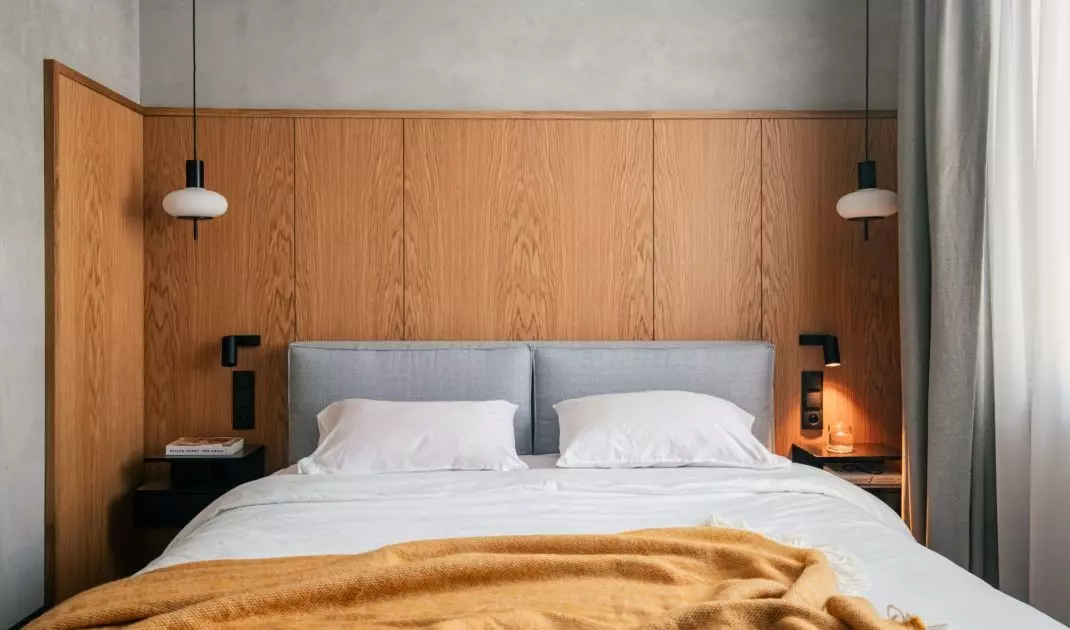 The bed is set against a high wooden wall, which visually warms the raw base of the bedroom