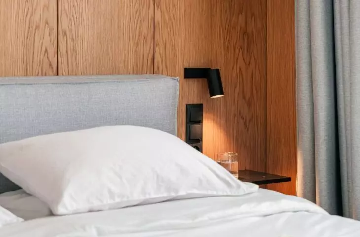 On two sides of the bed hung minimalist lamps with rounded milk glass shades