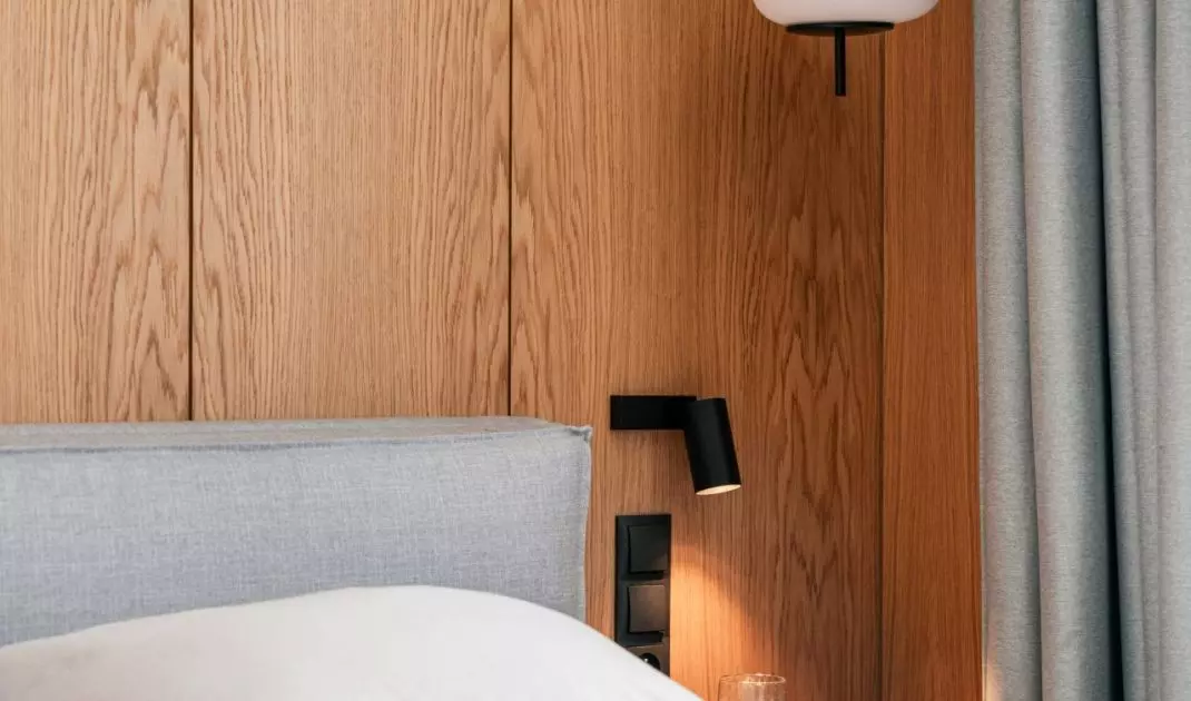 On two sides of the bed hung minimalist lamps with rounded milk glass shades