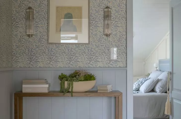 The wainscoting in the lower part of the corridor wall harmonizes with the patterned wallpaper, and the blue accents harmonize with the warm shade of the wood