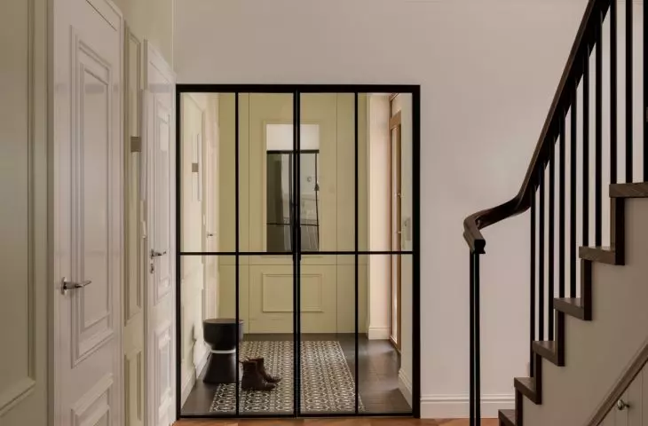 The hallway is separated from the other rooms by a glass door in a black metal frame 