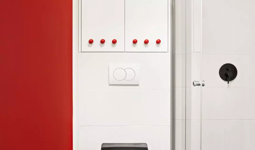 The white built-over toilet has been fitted with round red handles