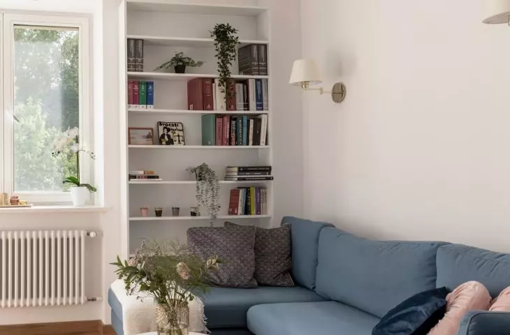 The living room has a navy blue sofa, over which hangs a modern lamp with several bulbs. Right in front of it its two tables with marble tops 