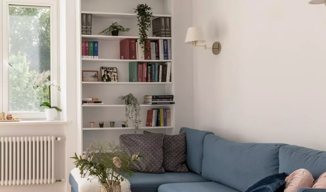 W salonie znajduje się granatowa sofa, nad którą zawisła nowoczesna lampa o kilku żarówkach. Tuż przed nią swoją dwa stoliki o marmurowych blatach 